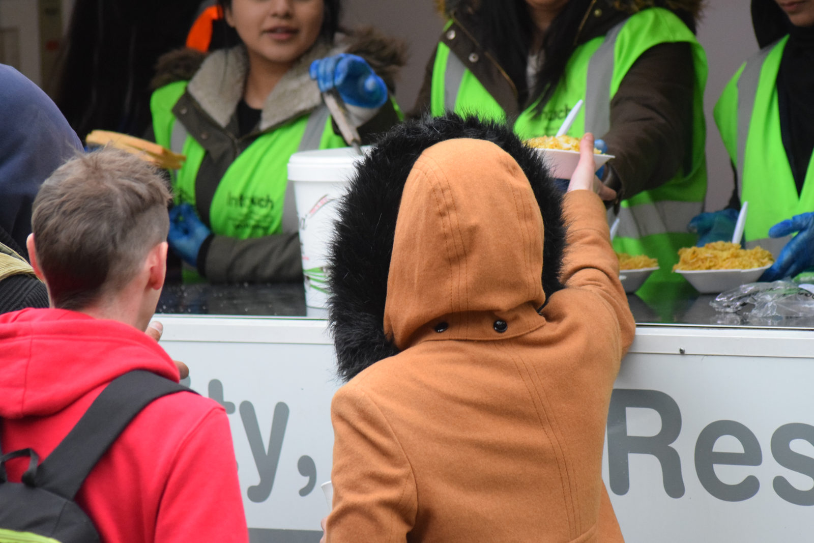 Volunteers in green InTouch high-visibility vests serving hot food to people from a mobile kitchen