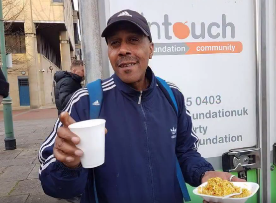 A man holding a cup of hot drink and a portion of food received from the InTouch mobile kitchen